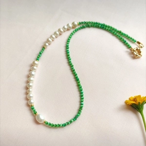 Detail of white baroque pearls and green cat eye beads necklace with gold clasp