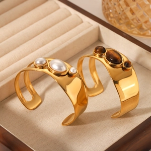 Detailed shot of open gold-plated bangles with natural tiger eye and white pearl accents