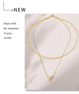 Close-up of a double-layered gold stainless steel necklace with bean pendant on stone