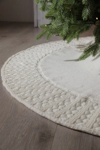 Detail of cream knitted Christmas tree skirt with textured pattern on wooden floor
