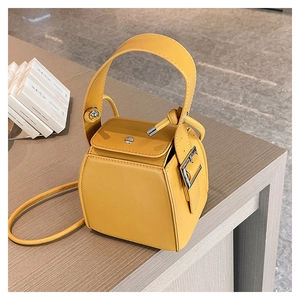 Detail of a chic yellow PU leather box bag on a wooden table with metallic hardware