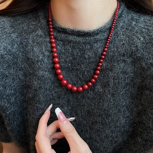 Détail du collier de perles dégradées rouges sur un pull gris, style luxueux