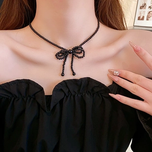 Close-up of a black beaded bow necklace worn by a model in a minimalist setting