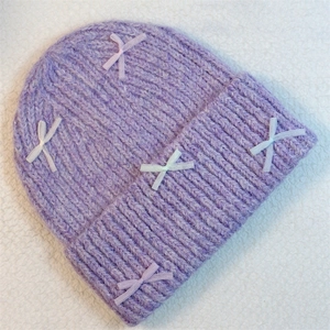 Detailed close-up of purple knit beanie featuring cute bow accents on soft plush texture