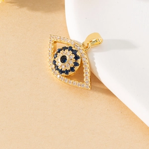 Detail of a gold Evil Eye pendant with blue and clear zircon crystals on white plate