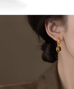 Close-up of elegant gold-plated earrings with oval tiger eye stone worn by a model