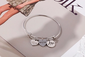 Detail of silver MOM and Love charms on an adjustable stainless steel heart bracelet