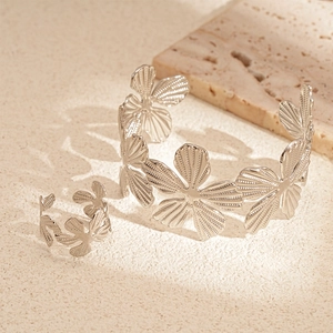 Detail of silver hollow flower jewelry set with textured petals on beige travertine