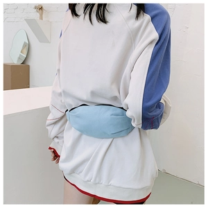 Close-up of light blue canvas waist bag worn by a model against a minimalist white wall