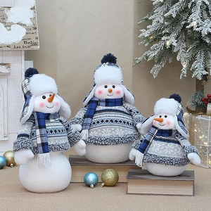 Tre pupazzi di neve natalizi blu e bianchi in abiti di maglia in un ambiente festivo