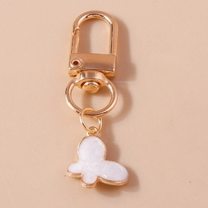 Golden butterfly keychain with white floral charm on a minimalist cream background