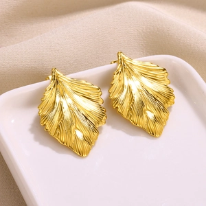 Macro view of gold stainless steel leaf earrings resting on a white porcelain tray