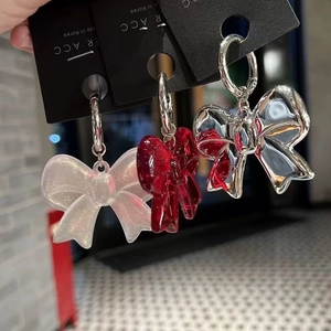 Three pairs of acrylic bow earrings in glitter, red, and silver on a black display card