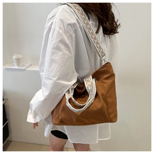 Brown nylon tote bag with patterned wide strap worn by a model in a side view