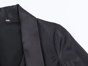 Detailed close-up of glossy black fabric texture and neat stitching on dress lapel