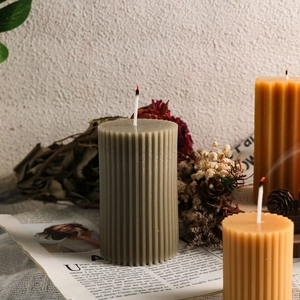 Velas de pilar acanaladas en verde salvia y ocre sobre base de madera con flores secas
