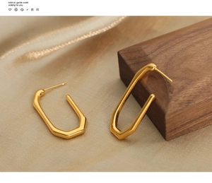 Close-up of geometric U-shaped 18k gold plated titanium earrings on silk and wood