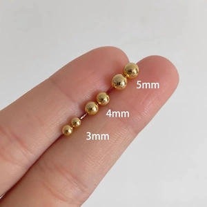 Boucles d'oreilles boules dorées minimalistes en tailles 3mm, 4mm et 5mm sur un doigt