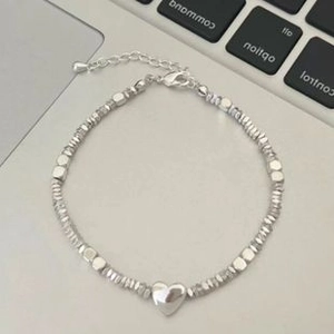 Detail of silver heart charm bracelet with small metallic beads on laptop keyboard