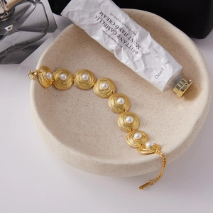 Detail of 18K gold-plated bracelet with spiral metal disks and white shell pearls