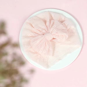 Detail of baby lace turban in soft pink with oversized bow on white minimalist base