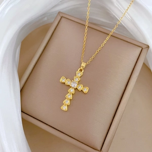 Elegant gold titanium cross pendant necklace with clear crystals on a beige jewelry box