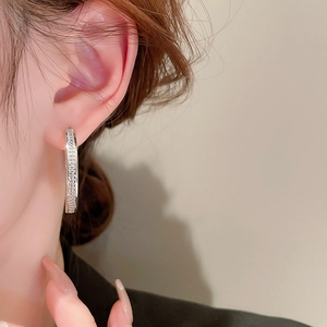 Macro shot of silver metal hoop earring with zircon inlay worn on earlobe