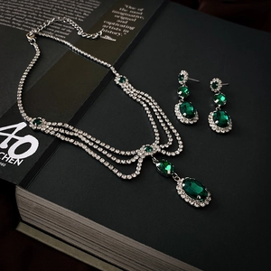 Vintage emerald and diamond layered necklace with matching earrings on a classic book