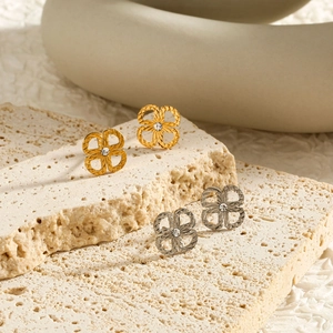 Macro shot of clover earrings with diamond-cut texture on minimalist beige stone surface