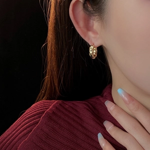 Detail view of gold-plated hammered hoop earrings worn by a model on a dark background
