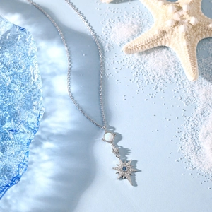 Detailed view of silver starfish necklace with opal and blue diamond on sand background