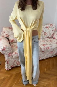 Dettaglio di maglia gialla chiara con lunghi fiocchi e maniche lunghe aderenti