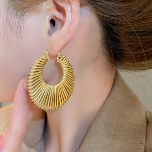 Gros plan d'une boucle d'oreille ronde tissée dorée portée par un mannequin élégant