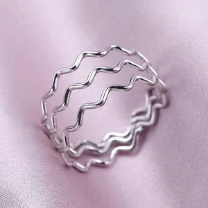 Macro view of silver triple-layered wavy ring on elegant soft purple silk background