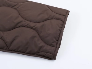 Détail de veste matelassée marron foncé montrant les coutures et la finition du poignet