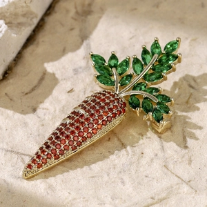 Golden carrot brooch with sparkling orange and green crystals on a beige stone surface