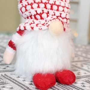 Detail of red and white knitted Christmas gnome with soft beard and striped hat on a mat