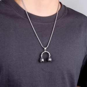 Close-up of a silver headphone pendant on a snake chain worn over a casual grey t-shirt