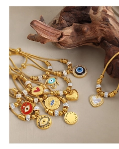 Detail of gold evil eye and heart charms on a titanium steel bracelet with wood backdrop