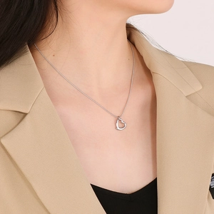 Close-up of silver hollow heart pendant necklace worn on neck with a beige blazer