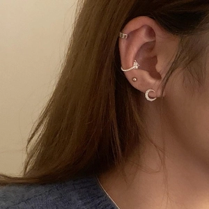 Detail of layered gold earrings with zircon ear cuff and textured C-shape design