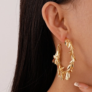 Close-up of oversized gold metallic hoop earrings with layered leaf-shaped fringe tassels