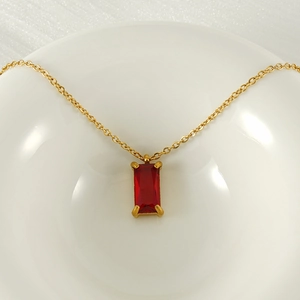 Detailed view of square red zircon pendant on a gold stainless steel necklace in a ceramic bowl