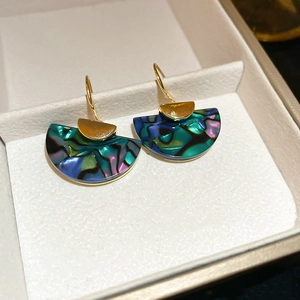 Detailed close-up of fan-shaped abalone shell earrings in a white jewelry box