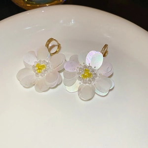 Macro shot of 3D floral earrings with iridescent sequins and gold hoop on light tray