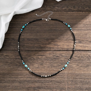 Handmade beaded necklace with black, white, and turquoise stone beads on dark wood background