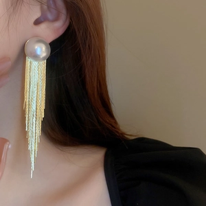 Macro detail of long gold chain tassel earrings featuring a large white round pearl