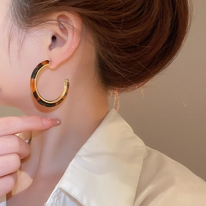 Close-up of tortoise shell resin C-shaped earrings with gold lining on female model