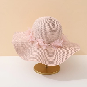 Détail du chapeau de paille rose avec bord ondulé, fleur en tulle et perles de nacre