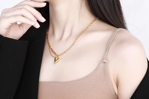 Dettaglio del ciondolo a cuore dorato su catena mista indossato con un blazer chic